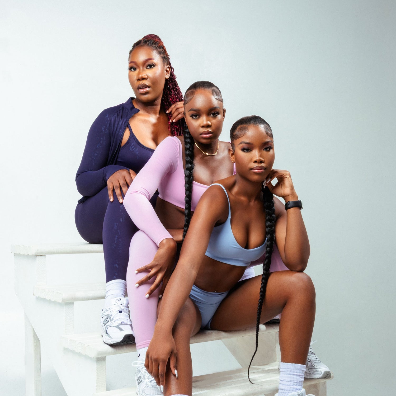 Three women sitting on a set of white steps against a light gray background